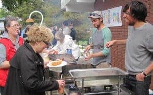 Photo of a past event. People are lined up and volunteers are serving food in front of the building at Highlands Park